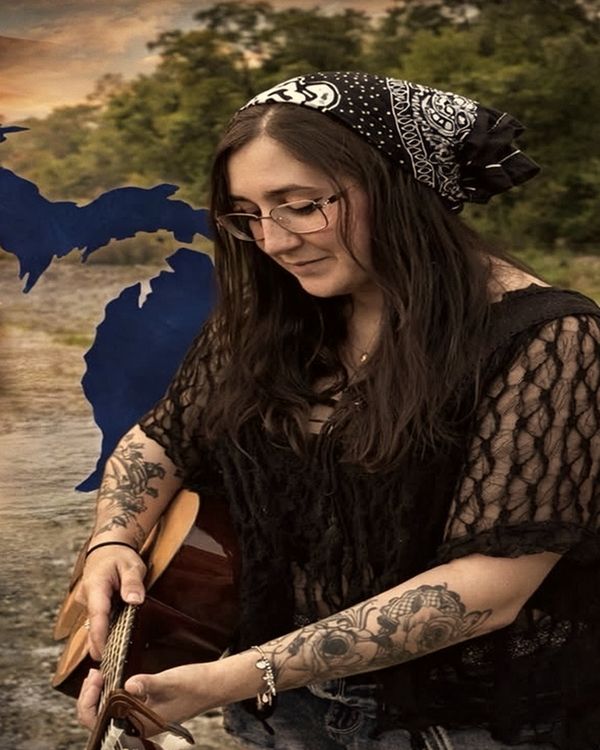 Trisha Marie in a bandana and glasses playing acoustic guitar, with a graphic of the state of Michigan behind her.